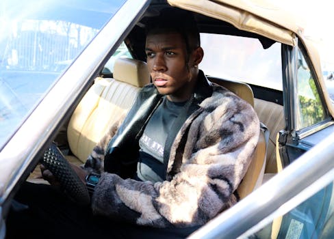 在一个晴朗的日子，一个穿着时髦皮大衣的人驾驶着一辆老式汽车