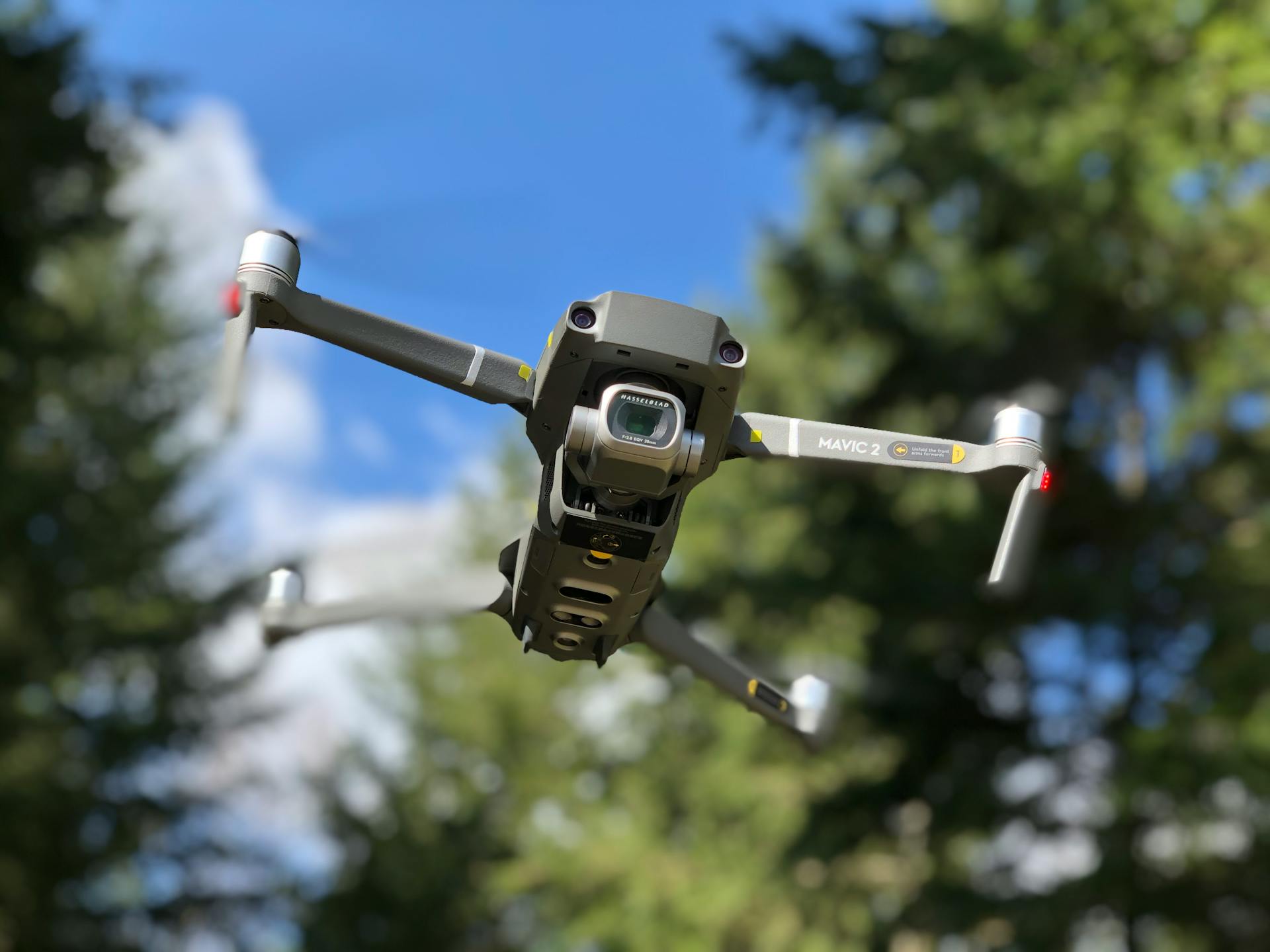 Close-up of drone in flight with blurred forest background, showcasing advanced technology.