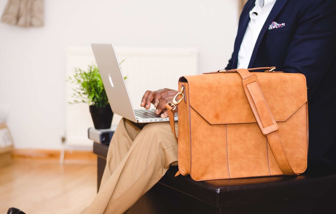 Free Person Wearing Blue Suit Beside Crossbody Bag and Using Macbook Stock Photo