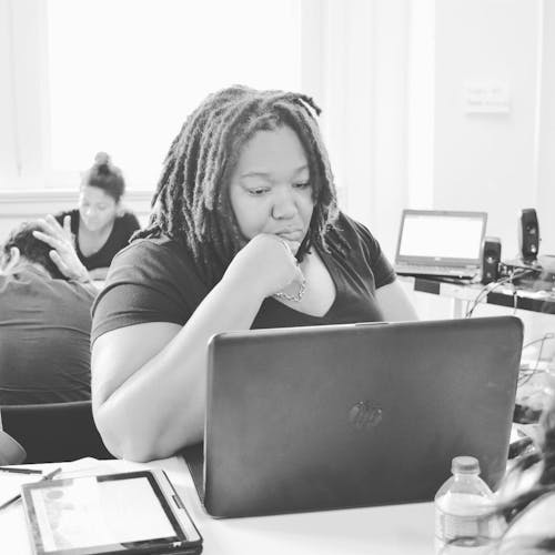 Grayscale Photo of Woman Wearing V-neck T-shirt Sitting in Front of Hp Laptop on Desk