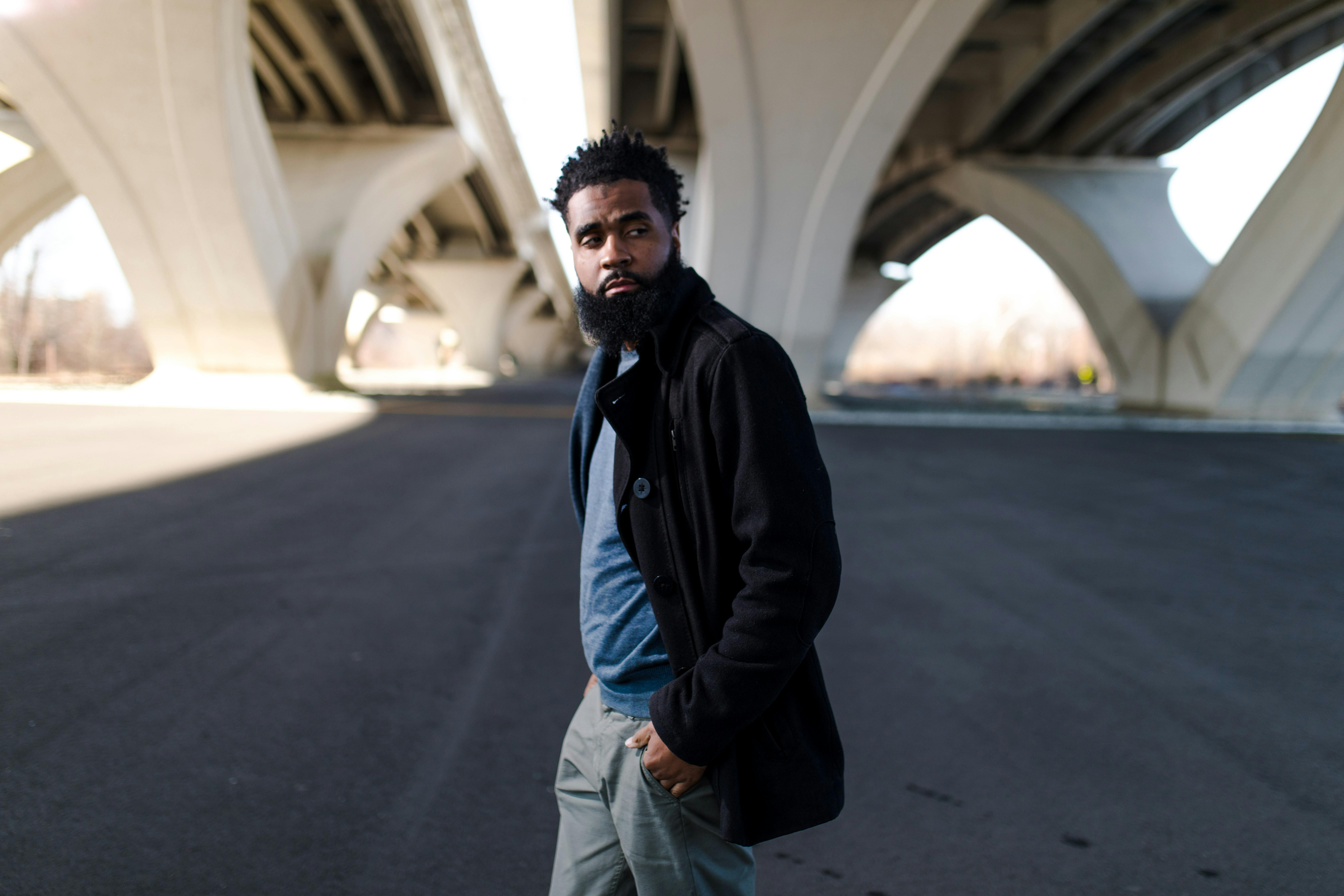 一位时尚前卫的非裔美国男子自信地在一座现代桥下摆姿势，展现城市风格