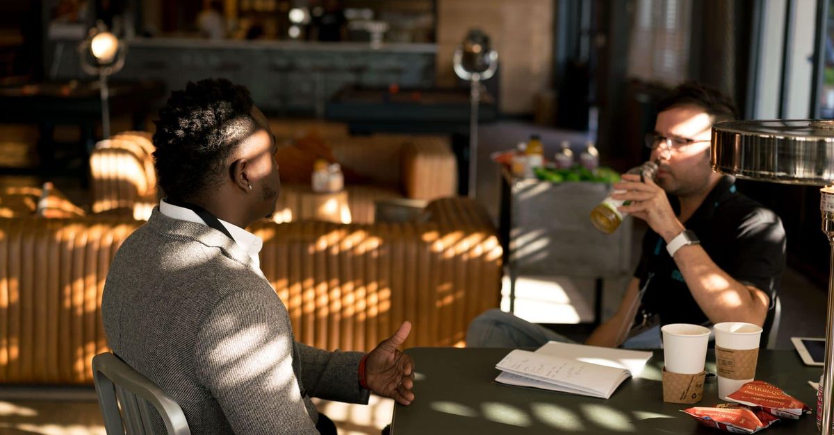 Two adults having a casual meeting with drinks in a modern indoor setting.