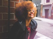 一位留着非洲发型、戴着眼镜的快乐女子在城市户外微笑