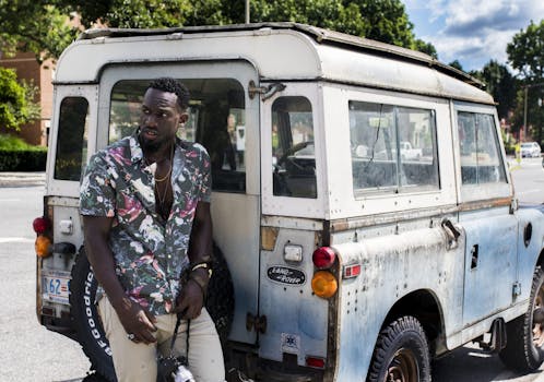 明亮的阳光下，一名时尚男子站在城市街道旁的一辆旧路虎边