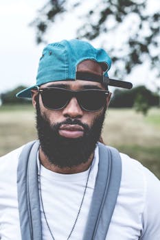 在一个阳光明媚的日子里，一位戴着太阳镜和帽子的时尚胡须男子站在户外