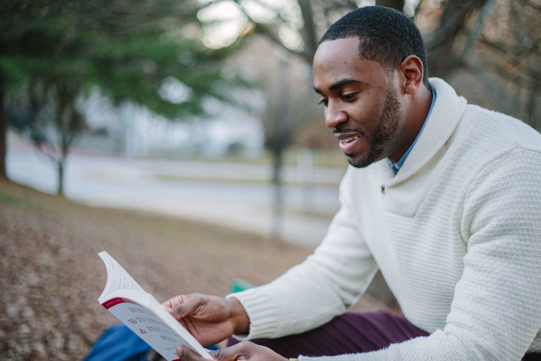 A young man enjoys reading in a serene park setting during the day.