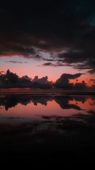 Vibrant sunset sky reflected on ocean water, creating a dramatic scene with clouds.
