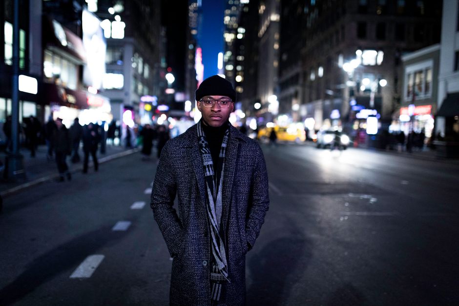 Man in stylish coat standing on a bustling city street at night.