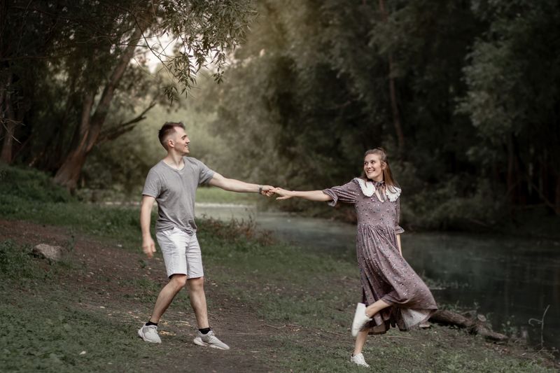 A joyful couple holding hands and walking in a lush green park during the day.