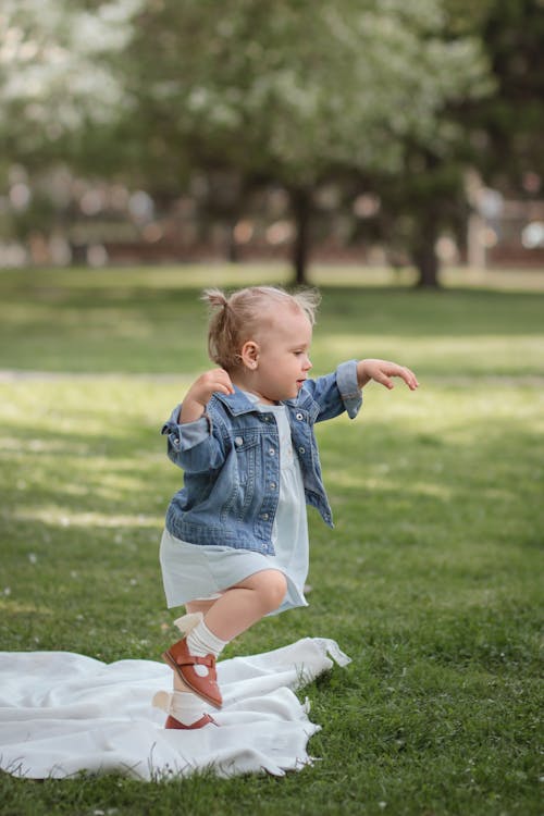 Free Girl in Blue Denim Dungaree Shorts and White Socks Running on Green Grass Field Stock Photo