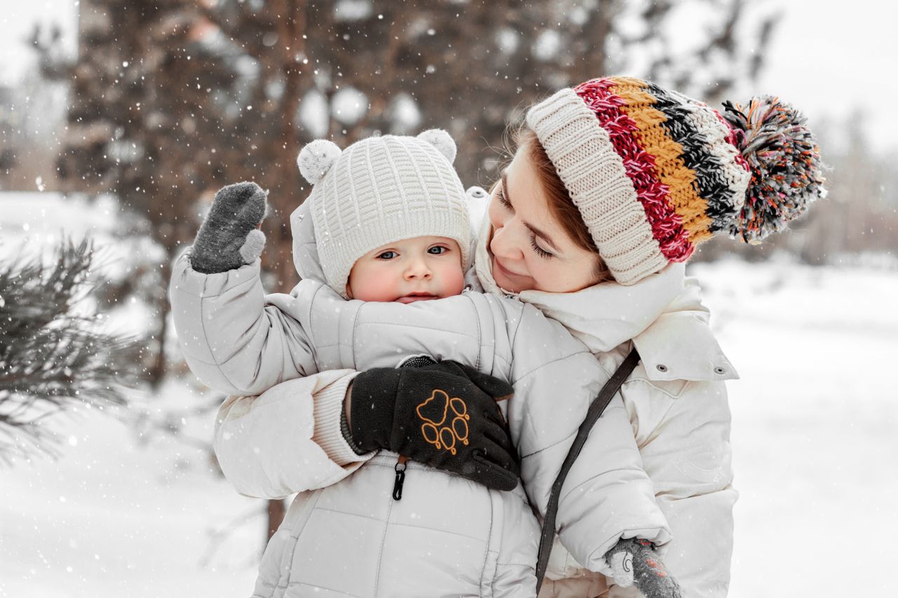 Mother holding a bundled-up toddler in falling snow