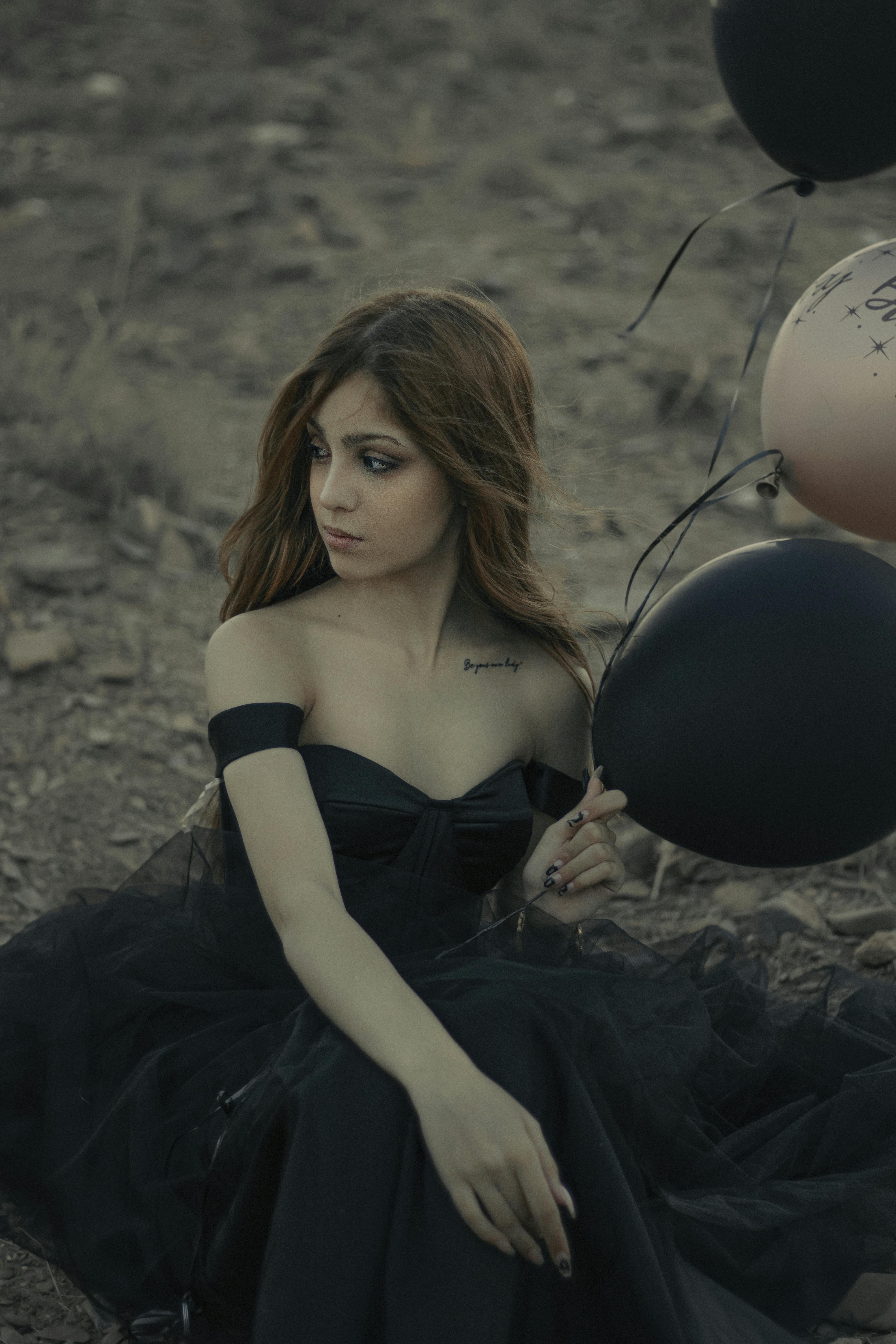 woman in black tube dress sitting on ground with balloons