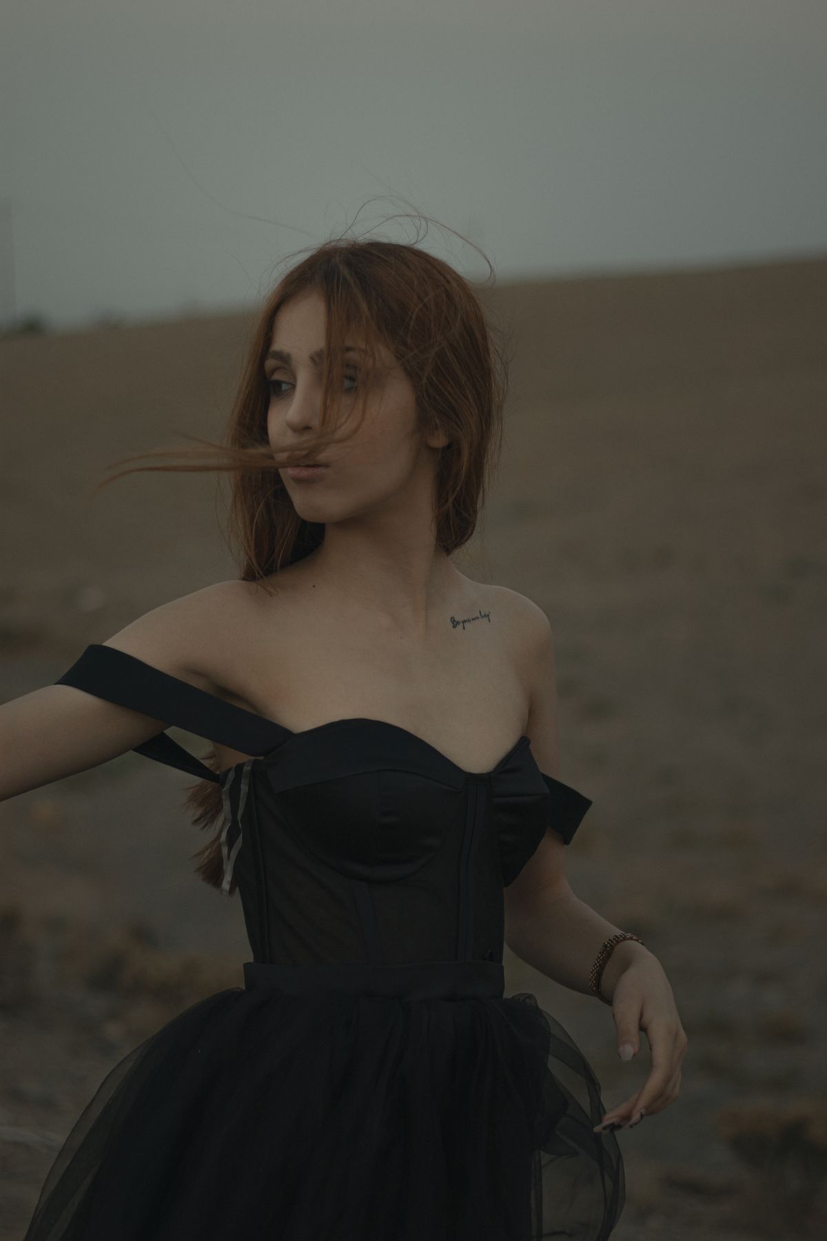 A woman in a black off-shoulder dress looking away — the sleek, minimalist off-shoulder
