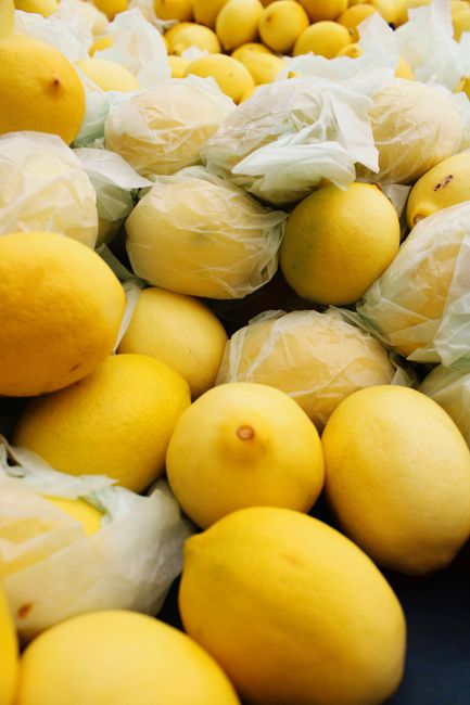 Close-up of fresh yellow lemons, some wrapped in paper, highlighting their vibrant color.