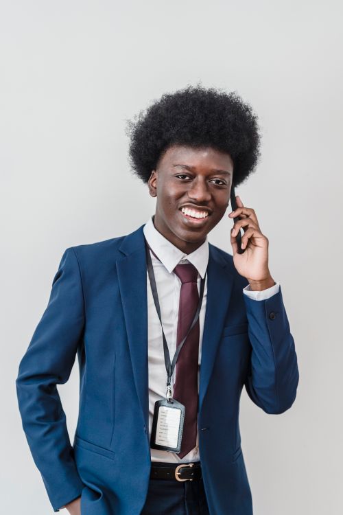 Free Smiling businessman with an afro hairstyle talking on mobile phone in a formal suit against white background. Stock Photo