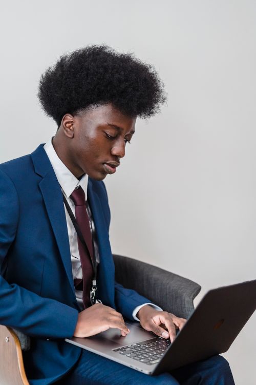 Free A young man in a blue suit using a laptop indoors, focused on work. Stock Photo
