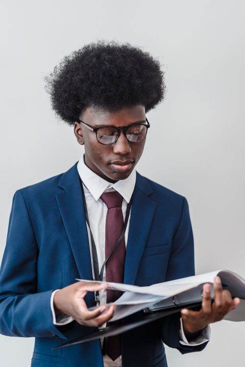Free Businessman in a blue suit reviewing documents indoors, standing against a white background. Stock Photo