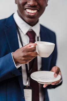 Smiling businessman in a suit holding a coffee cup and saucer, enjoying a break.