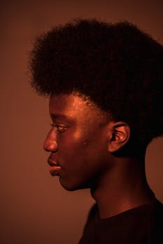 Profile view portrait of a man with afro hair against a warm orange background.