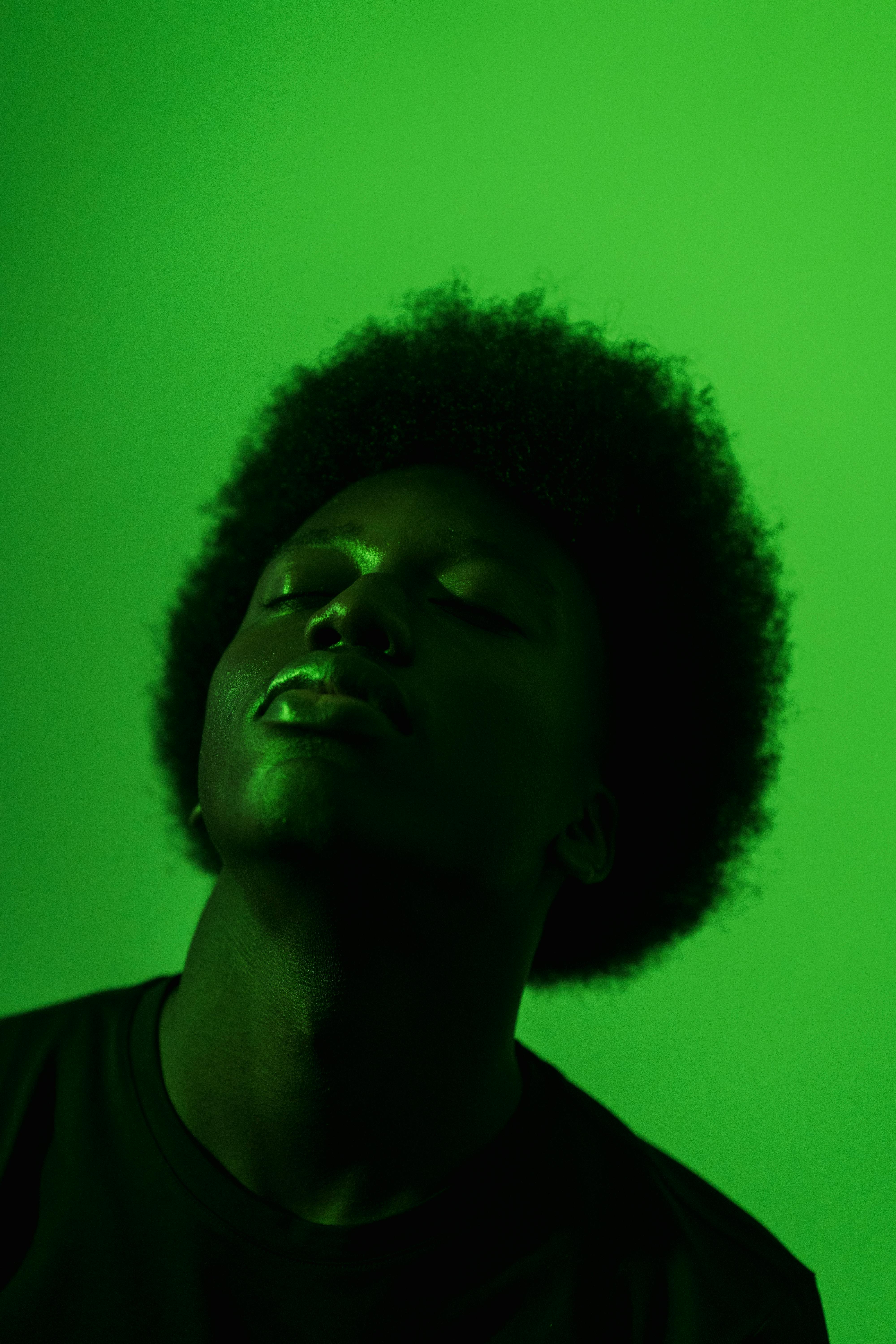 Artistic portrait of a man with afro hair in green monochrome lighting, eyes closed.