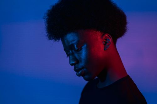 Free Artistic portrait of a man with Afro hair against a blue and red illuminated background. Stock Photo