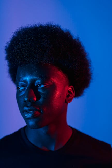 Moody studio portrait of a man with an afro, illuminated by contrasting red and blue lighting.