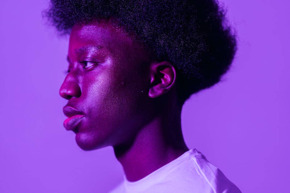 Profile portrait of a young man with afro hair against a vibrant purple background.