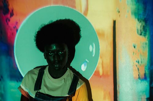 Free Portrait of a young black adult with afro hair in front of a vivid abstract background. Stock Photo
