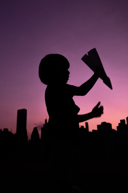 Free A child plays with a paper airplane against a vibrant sunset, creating a compelling silhouette. Stock Photo