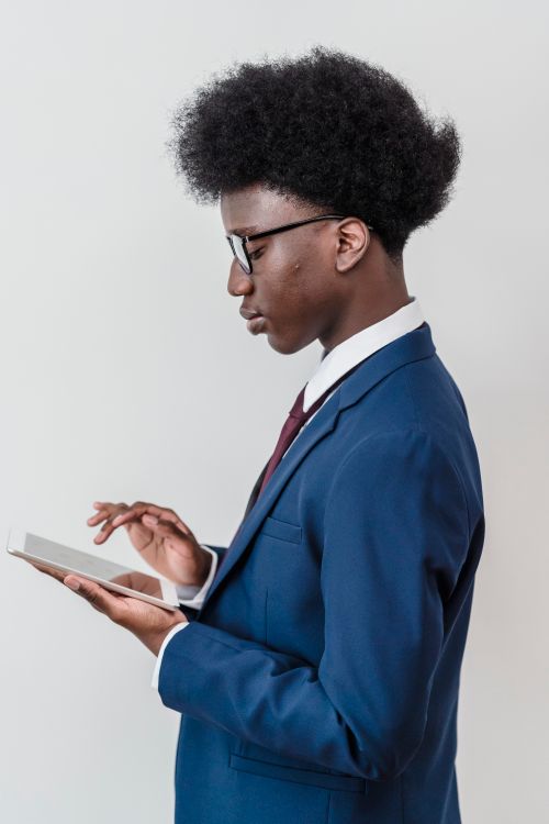 Free Side view of a young black man in a blue suit using a tablet against a white background. Stock Photo