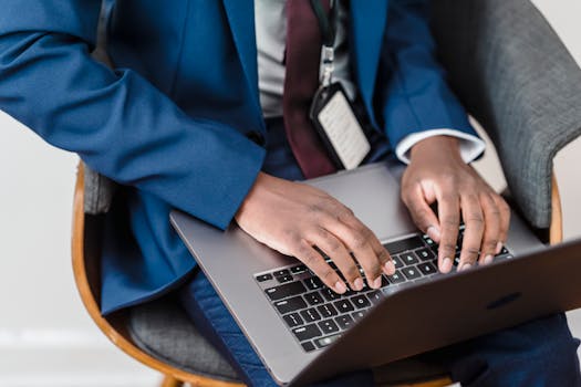 Close-up of a businessman in a blue suit working on a laptop indoors.