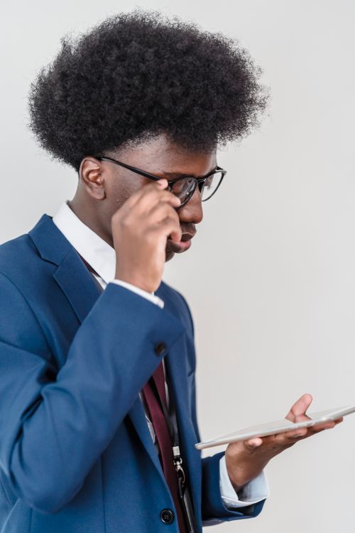 Free Young man in a suit using a digital tablet indoors, adjusting eyeglasses. Stock Photo