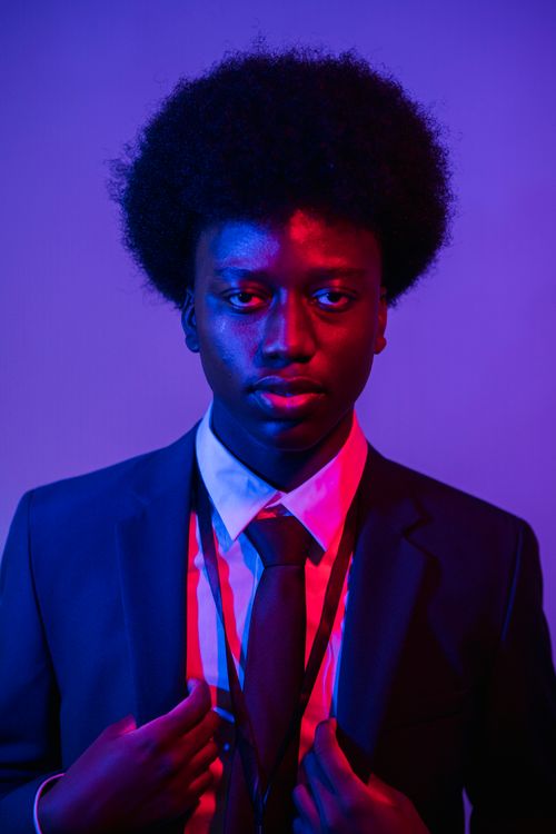 Free Portrait of a young man with afro hairstyle in a suit, highlighted by vibrant lighting. Stock Photo