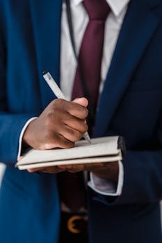 Businessman in a suit writing notes in a notebook, close-up view.