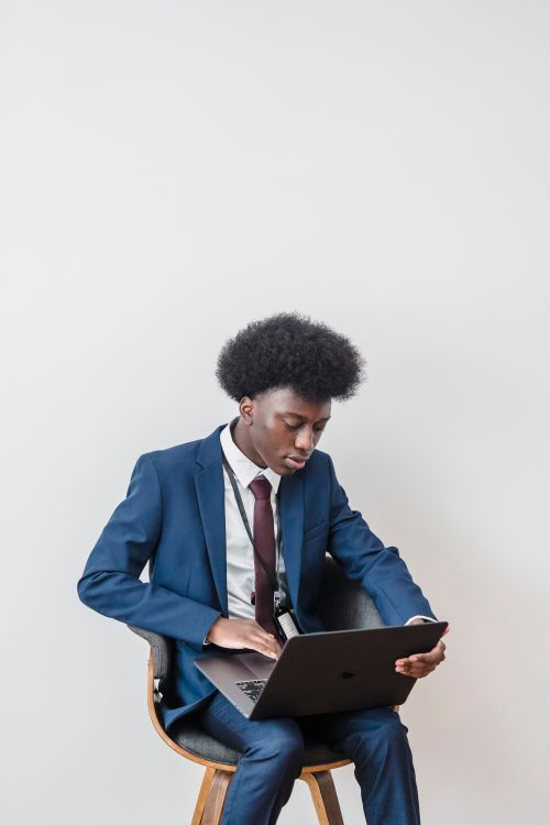 Free A young man in a blue suit working remotely on a laptop indoors, showcasing modern work culture. Stock Photo