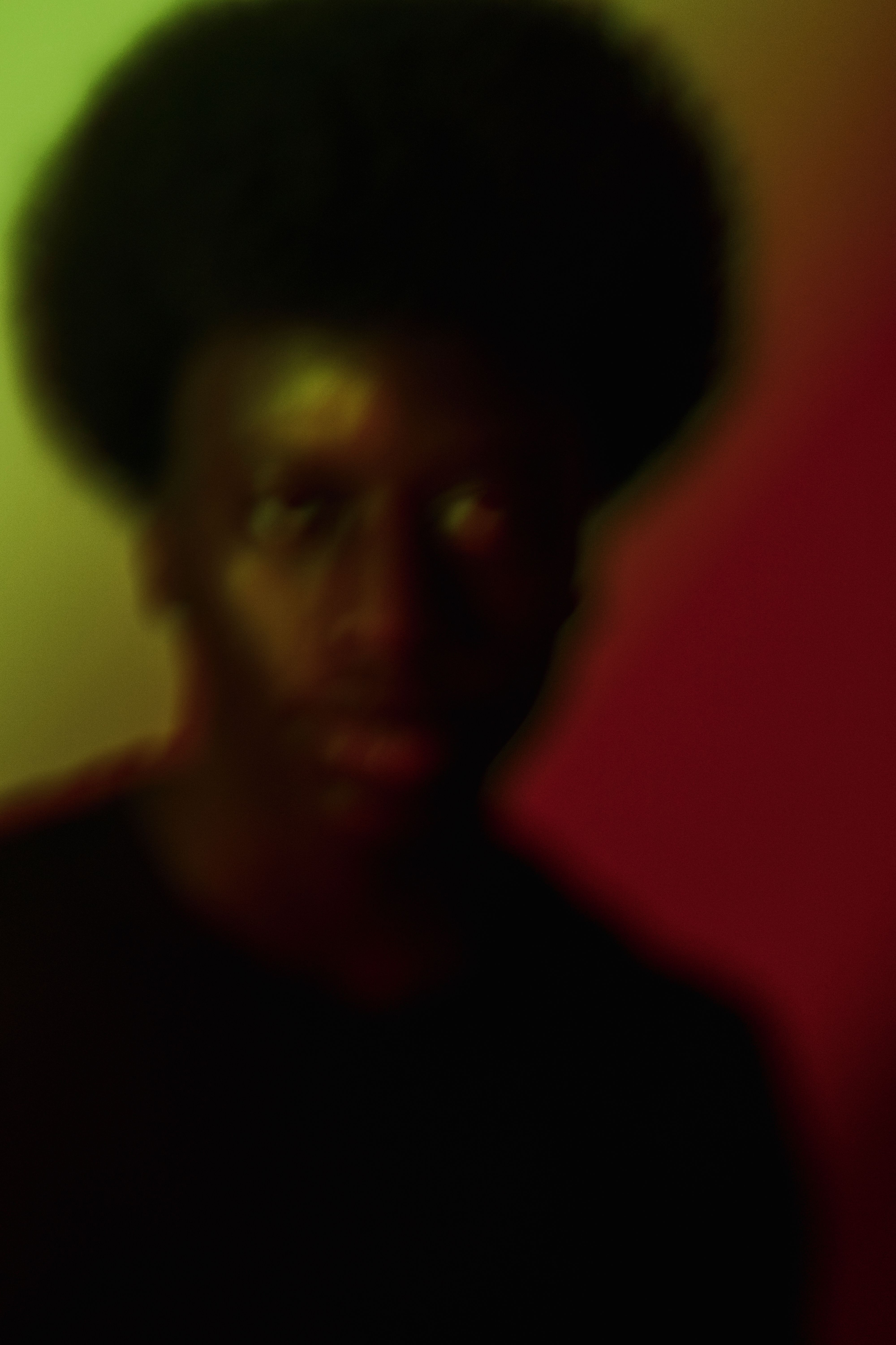 Blurry artistic portrait of a person with afro hair, featuring vibrant colors and unique lighting.