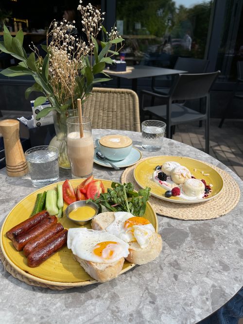 Free Delicious outdoor brunch with fried eggs, sausages, fresh salad, and cappuccino on a sunny day. Stock Photo