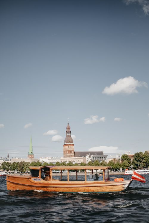 Free A scenic view of a wooden boat cruising on the Daugava River with Riga's skyline in the background. Stock Photo