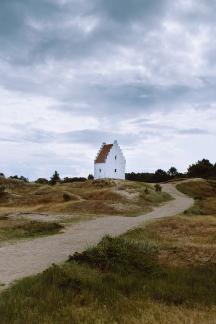A scenic view of the buried church in Skagen, Denmark, under a cloudy sky.