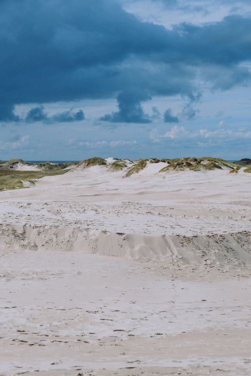 Free Sandy desert landscape with rolling dunes beneath a dramatic cloudy sky, captured during the day. Stock Photo