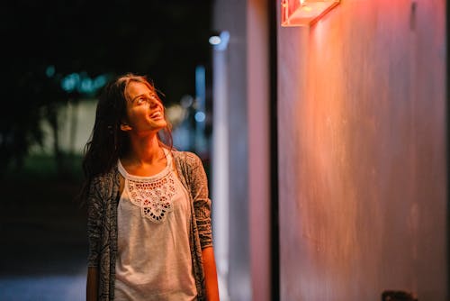 Free Woman in Gray Cardigan Standing Near Wall during Nighttime Stock Photo