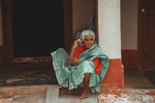 Free Senior woman sitting barefoot in a traditional sari at an entrance with a thoughtful expression. Stock Photo