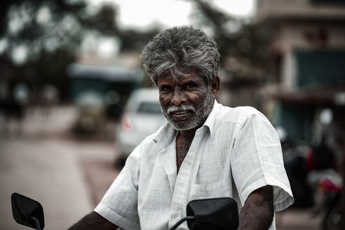Free Close-up of a senior man in a white shirt, captured with a shallow focus against a blurred background. Stock Photo