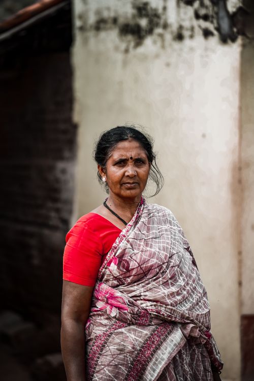 Free An elderly woman wearing a traditional saree stands outdoors with a blurred background. Stock Photo