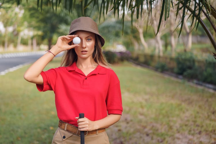 Woman In Red Polo Shirt And Brown Pants Holding Golf Ball