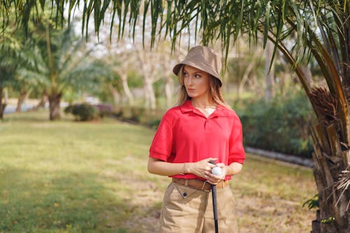 Free Woman in Pink Polo Shirt and Brown Hat Standing Near Green Grass Field Stock Photo