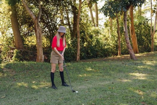 Woman golfer in bucket hat preparing to swing on a lush, green course.