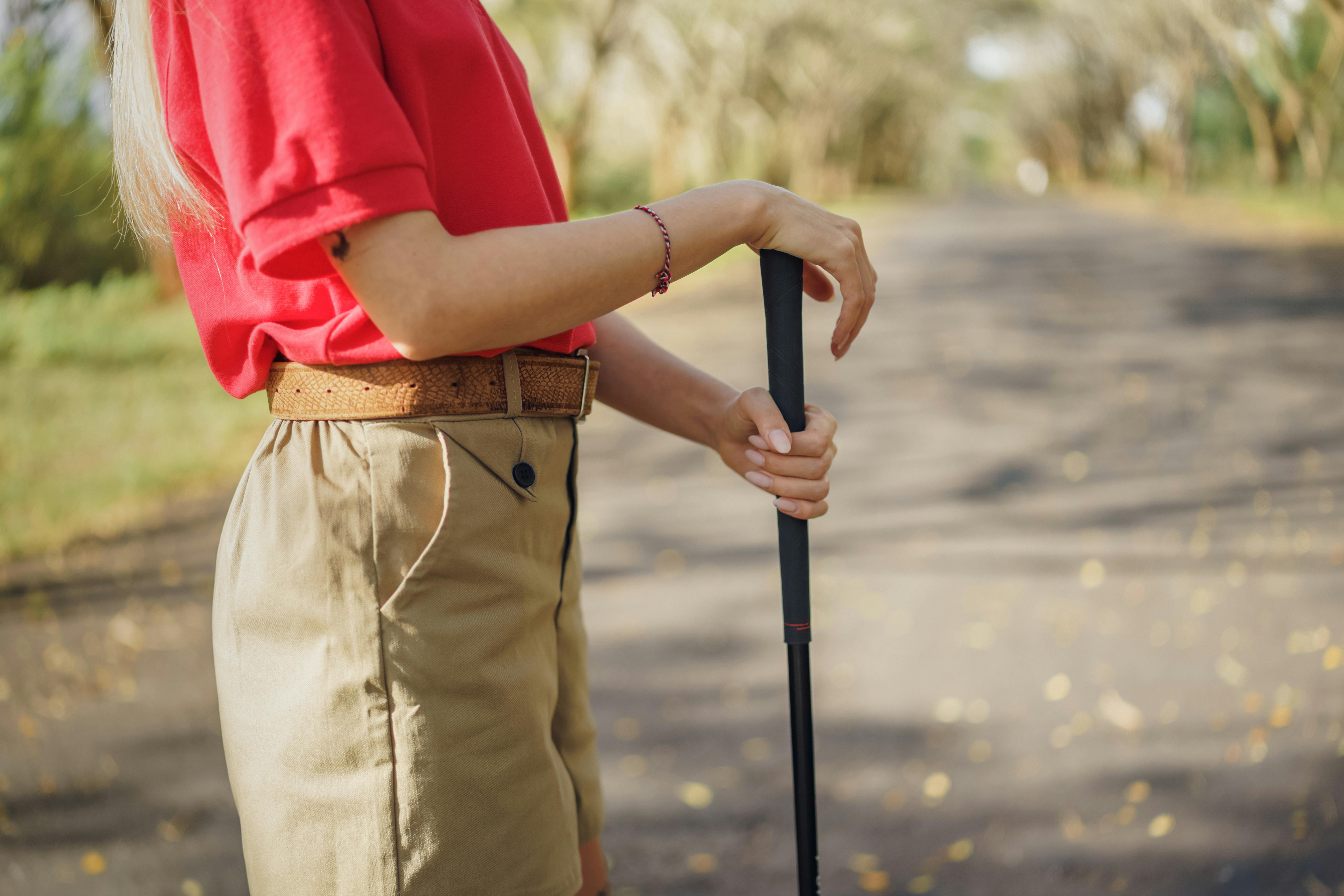 A close-up of a person in a red shirt holding a golf club outdoors on a sunny day.