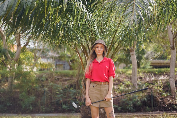 Woman In Red Polo Shirt Standing Near Palm Tree While Holding A Golf Club