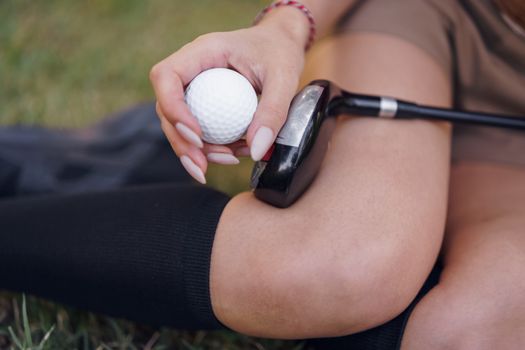 A woman sitting with a golf ball and club, focusing on sports gear in casual setting.